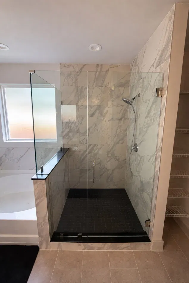 Frameless glass shower with marble look porcelain tile and black shower pan by CNB Renovations